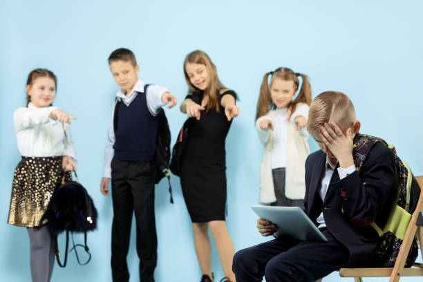 der kleine junge sitzt allein auf dem stuhl und erleidet einen akt des mobbings. - bullying child teasing little boys stock-fotos und bilder