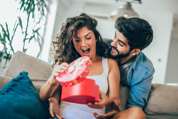 istock Smiling man surprises his girlfriend with present at home 1138121356