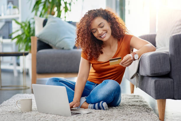Nothing makes shopping easier than credit Shot of a young woman using a laptop and credit card in the living room at home financial wellbeing stock pictures, royalty-free photos & images