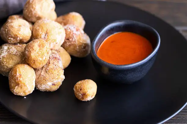 Photo of Famous Canary Islands dish, Papas Arrugadas (wrinkly potatoes with salt) and Mojo picon (red  spicy sauce) on wood table in local restaurant.