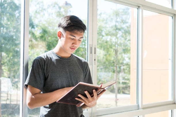 istock Education Learning Studying concept : Attractive Happy handsome Asian Young man enjoy reading book for preparing final test exam at school building windows on vacation time in summer day. 1138127152