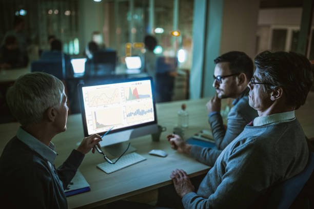 istock Business colleagues talking about charts while working on desktop PC at dark office. 1138132628