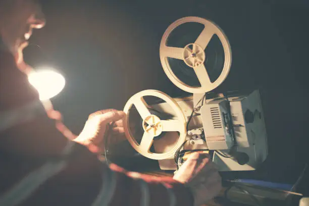 Photo of man set up film reel on vintage 8mm movie projector in dark room