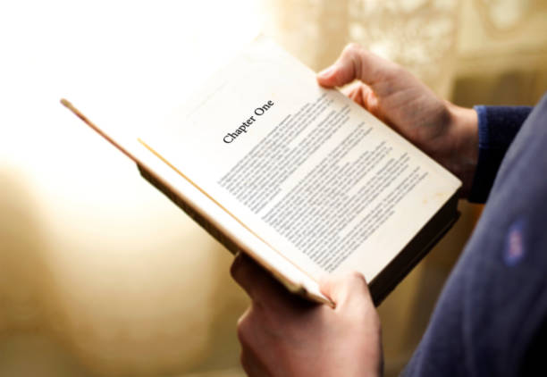 man's hand on book page with title "chapter one" - chapter one imagens e fotografias de stock