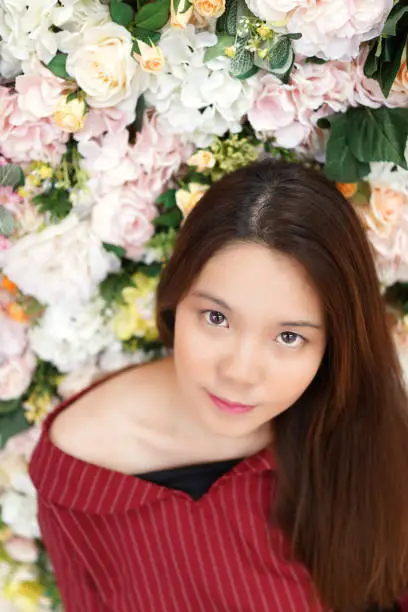 Beautiful Asian young girl with fresh clean skin and pretty eyes in front of  roses floral background. Vertical