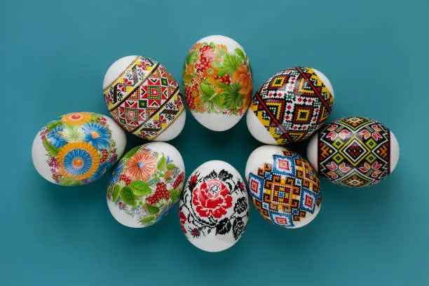 Photo of Close-up of multicolored traditional motifs on Easter eggs. Festive card of colorful easter eggs on blue background. Copy space. Easter tradition.