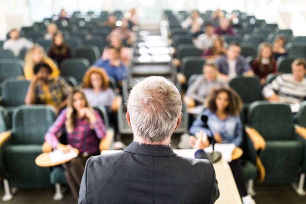 istock Back view of a senior professor talking on a class to large group of students. 1138138038