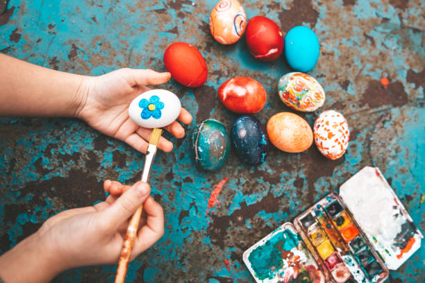 Overhead view on Childs hand painting easter eggs on old blue vintage background