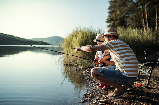 Un padre maduro con un pequeño hijo niño que pesca al aire libre por un lago. photo