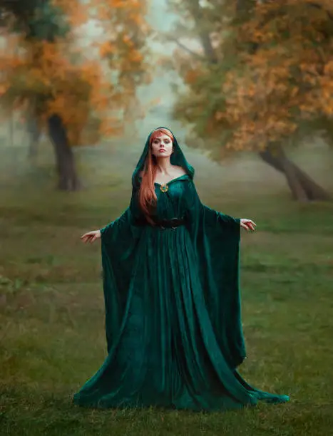 runaway princess with red blond long hair dressed in a green emerald expensive velvet royal cloak-dress with a precious brooch, the girl got lost in a dark foggy forest, fell into a trap, art photo.