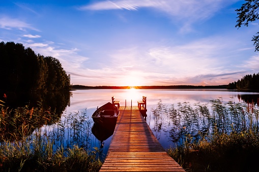 Muelle de madera con barco de pesca al atardecer en un lago en Finlandia photo