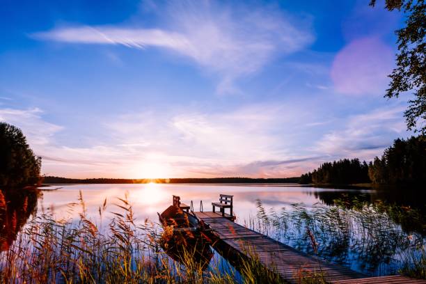 деревянный пирс с рыбацкой лодкой на закате на озере в финляндии - romance lake chair sunset стоковые фото и изображения