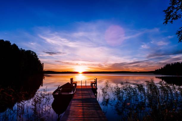 деревянный пирс с рыбацкой лодкой на закате на озере в финляндии - romance lake chair sunset стоковые фото и изображения