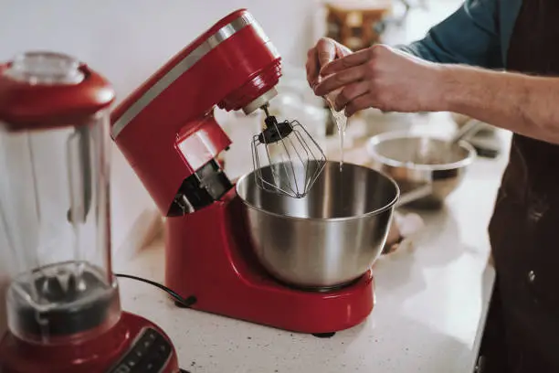 Modern red electric standing mixer with a big metal bowl and a man pouring raw egg into it