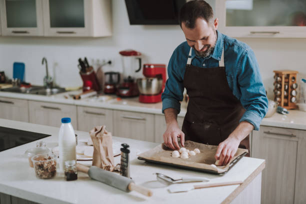 istock Cheerful man smiling while putting pastry on the sheet pan 1138147687
