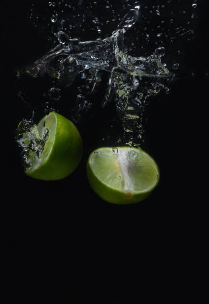 Lime green fruit that is falling and has water spreading with a black background.