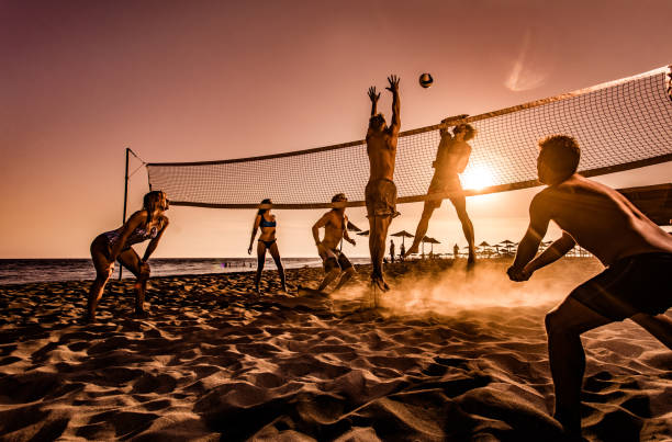 große gruppe von freunden, die beachvolleyball bei sonnenuntergang spielen. - strand volleyball stock-fotos und bilder