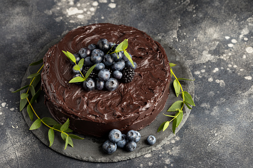 Tasty chocolate cake with berries and green leafs on dark background. Concept of birthday holiday food. Free space for text