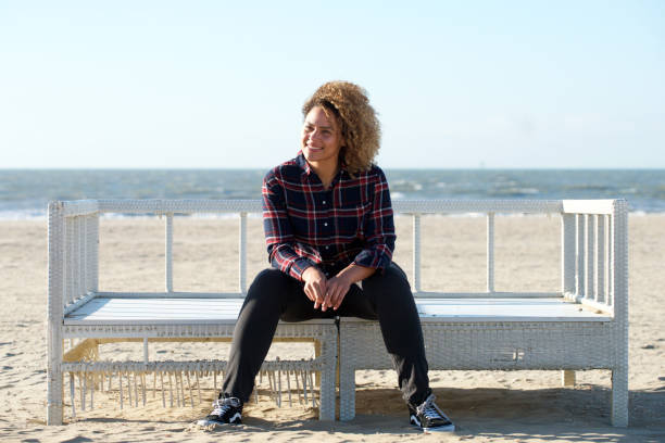 istock happy young woman sitting on bench at the beach 1138155351