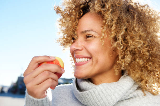 リンゴを保持している健康な若いアフリカ系アメリカ人女性のサイド肖像 - women eating fruit food ストックフォトと画像