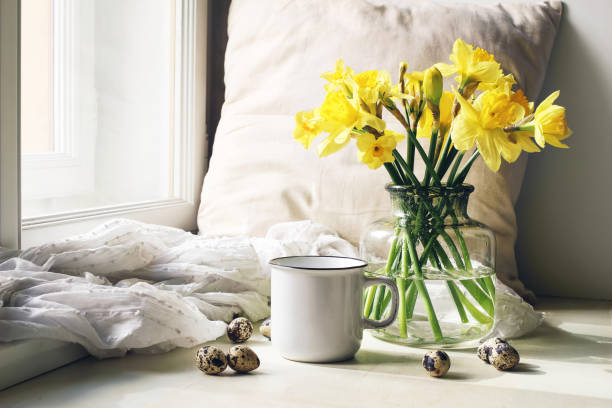 semana santa acogedora, escena de la vida todavía. taza de café, plato de madera, huevos de codorniz y jarrón de flores en la alféizar de la ventana. composición floral con narcisos amarillos, narciso. foto vintage estilo femenino. - yellow easter daffodil religious celebration fotografías e imágenes de stock