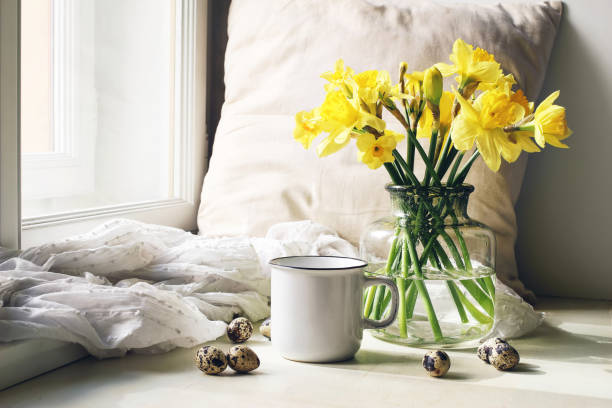 cozy easter, spring still life scene. mug of coffee, wooden plate, quail eggs and vase of flowers on windowsill. floral composition with yellow daffodils, narcissus. vintage feminine styled photo. - daffodil flower yellow vase imagens e fotografias de stock