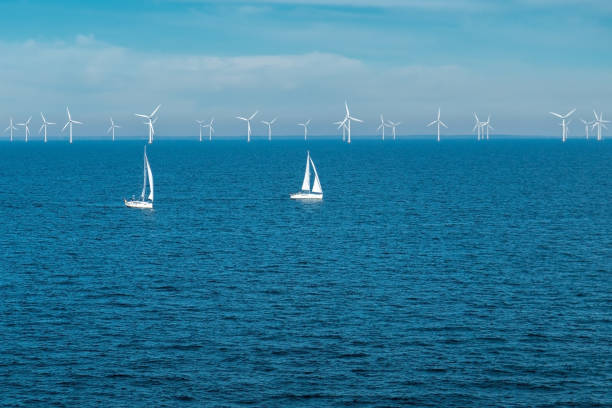 Alternative energy - row of offshore wind turbines and yachts at sea, green energy windmill generators at sea stock photo