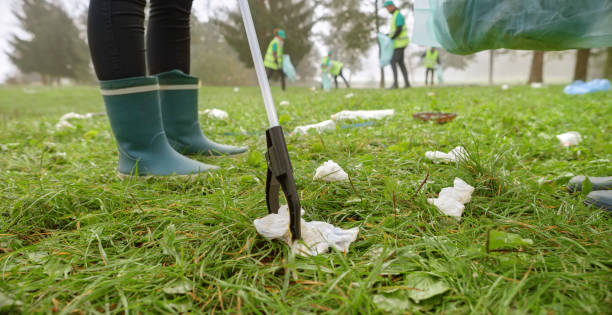 Low section of woman in wellington boots picking up rubbish with waste picker in park.
