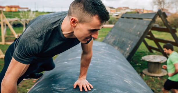 Man in an obstacle course climbing a drum Male participant in an obstacle course climbing a drum military camp stock pictures, royalty-free photos & images