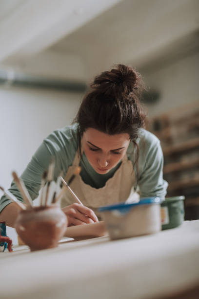 istock Charming young woman in apron painting pottery at workshop 1138167290