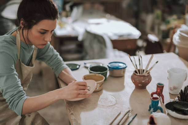 istock Beautiful brunette lady in apron painting pottery at workshop 1138167301
