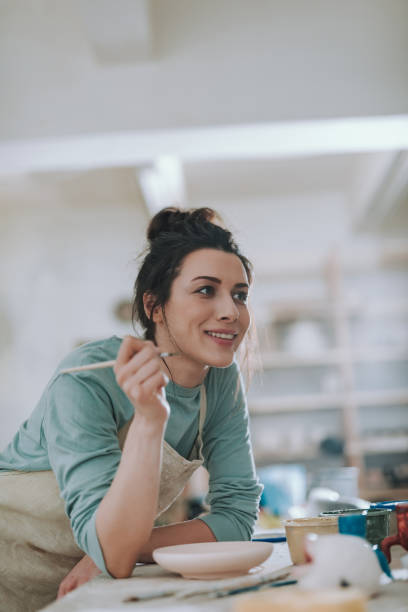 istock Joyful young woman painting pottery at workshop 1138167310