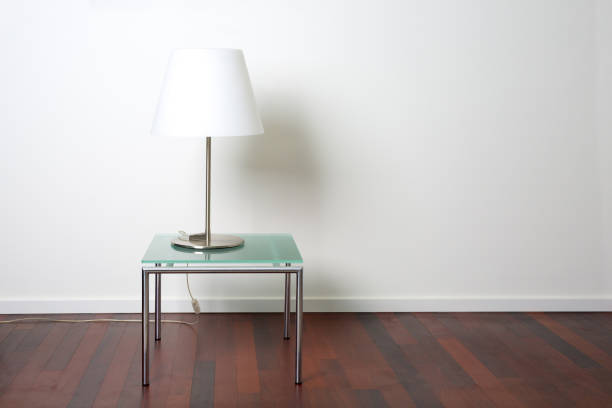 Modern lamp on glass table, wooden floor and white plastered wall with copy space.