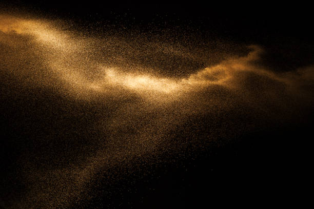 Photo of Golden sand explosion isolated on black background. Abstract sand cloud.