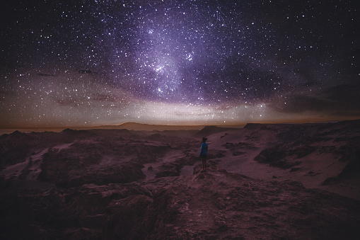 Woman enjoying stargazing under the night sky with million of stars and Milky Way at beautiful canyon on Atacama Desert in Chile
