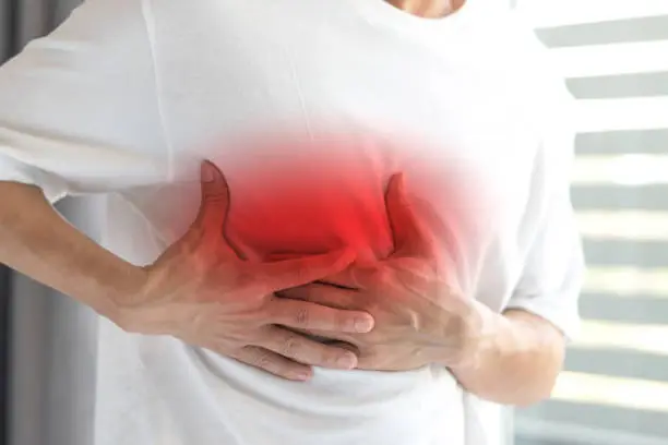 Photo of Man's hands on his chest in white shirt with red spot as suffering on chest pain. Male suffer from heart attack,Lung Problems,Myocarditis, heart burn,Pneumonia or lung abscess, pulmonary embolism day