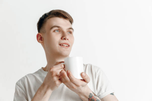 je prends une pause-café. jeune homme beau retenant la cuvette de café, souriant tout debout contre le fond gris - male mug shot cut out one person photos et images de collection