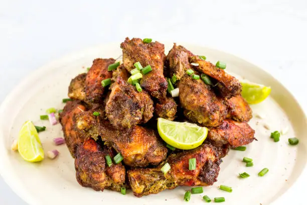 Pile of Jamaican Jerk Chicken Wings on a Plate with Lemon. Popular Chicken Wings Appetizer, Dry Rub Chicken Up Close Photo.