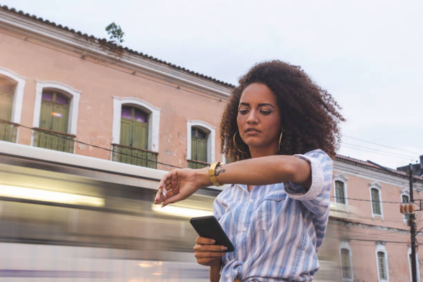 young woman waiting for a taxi ordered via mobile app at city in the rush hour - waiting women clock boredom imagens e fotografias de stock