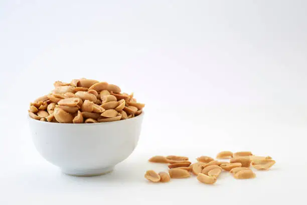 Small bowl of roasted salted peanuts on white background