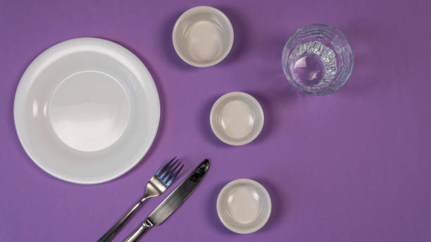 istock Concept diet - empty dishes, fork and knife on purple background. White dishes and glass cup 1138183147