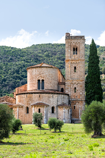 Abbey of Sant Antimo former Benedictine monastery vertical view in comune of Montalcino, Tuscany in summer with olive trees mountain