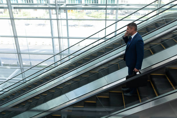 istock Businessman talking on mobile phone while moving down on escalator 1138185774