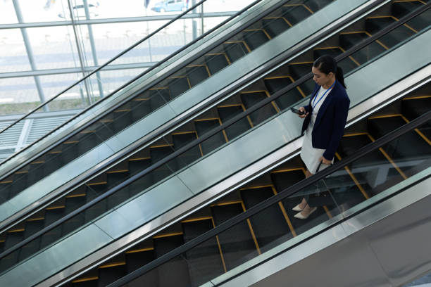 istock Businesswoman using mobile phone while moving down on escalator 1138185812
