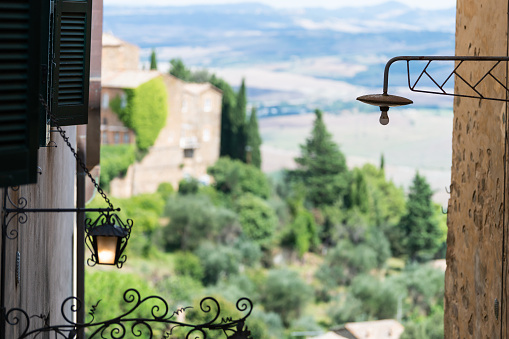 Montalcino, Italy historic medieval town village in Tuscany on sunny day and nobody with framing view of rolling hills and mountains between buildings and lantern lamp