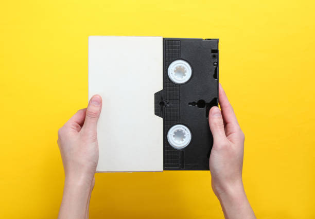 woman hands holding videocassette in cover, videotape on a yellow background.top view, minimalism. - video cassette tape imagens e fotografias de stock