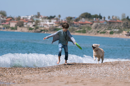 Happy boy running wit her dog on the beach.