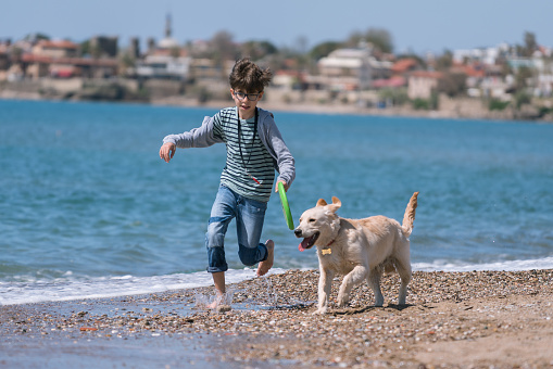 Happy boy running wit her dog on the beach.