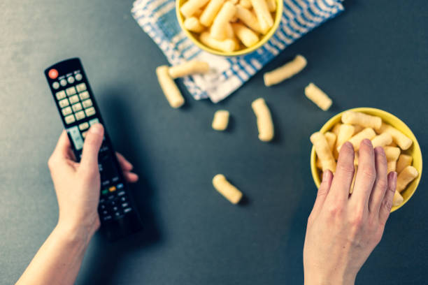 istock Person with TV remote watching tv and eating chips 1138199338