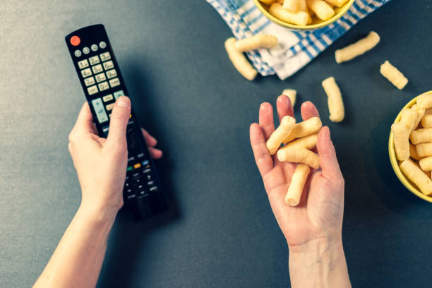 istock Person with TV remote watching a tv and eating chips 1138199371